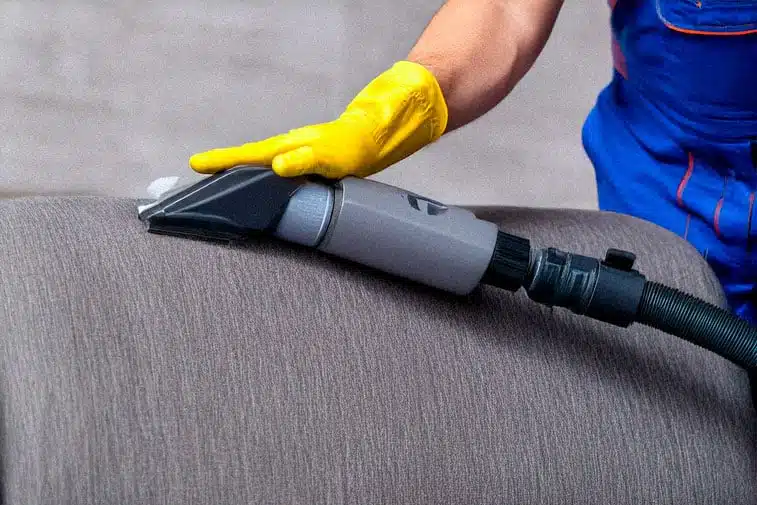 A cleaning technician's from daso green technologies hand is using a damp cloth on a sofa upholstery in a living room.